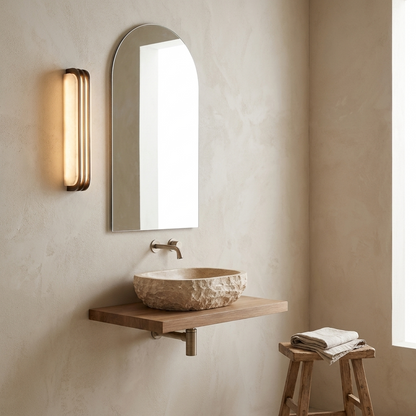 Slim marble wall sconce beside an arched mirror in a minimalist stone bathroom