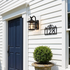 Black farmhouse lantern outdoor wall light on white clapboard facade by navy front door