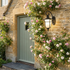 Black classic lantern outdoor wall sconce on honey stone cottage wall beside sage green door