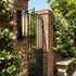 Slim exterior wall sconce on a red brick garden wall with climbing jasmine in bright daylight