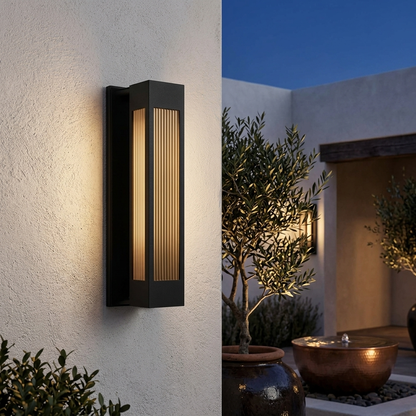 Exterior LED wall sconce glowing at night on a plastered courtyard wall with olive trees