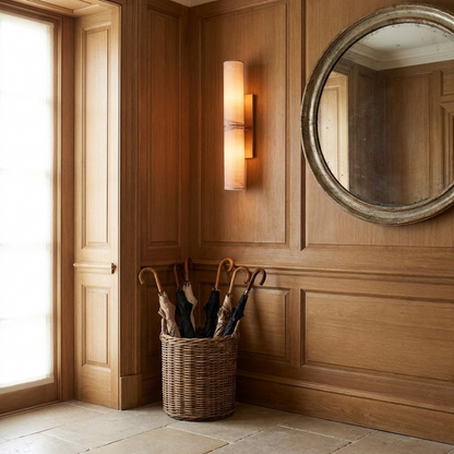 Copper and marble wall light glowing in a panelled entryway with limestone floor
