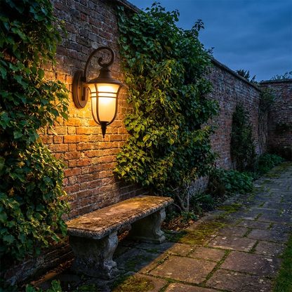 Lantern outdoor wall light on ivy clad brick boundary wall at blue hour with warm glow