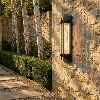 Black steel outdoor wall light on limestone garden path wall at golden hour