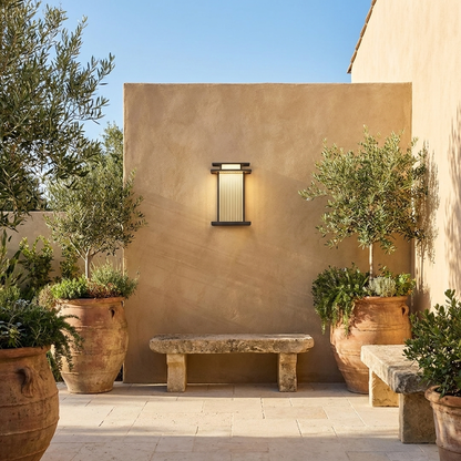 Black ribbed glass outdoor wall sconce on sand rendered courtyard wall with olive planters