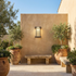 Black ribbed glass outdoor wall sconce on sand rendered courtyard wall with olive planters