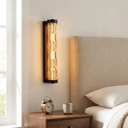 Amber glass linear wall sconce beside a linen headboard in a primary bedroom