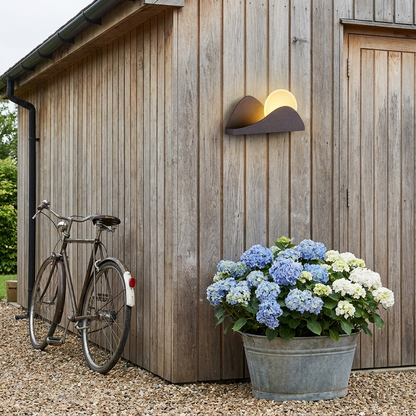 Solar sunrise wall light on a timber clad garden outbuilding with bicycle and planter