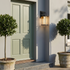 Black geometric lantern outdoor wall sconce on grey rendered facade beside sage front door
