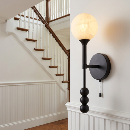 Isaure matte black wall sconce in the entry foyer of a colonial style home with white wainscoting and a staircase