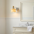 Lucienne Glass Drum Wall Sconce in Beige beside a bathroom mirror