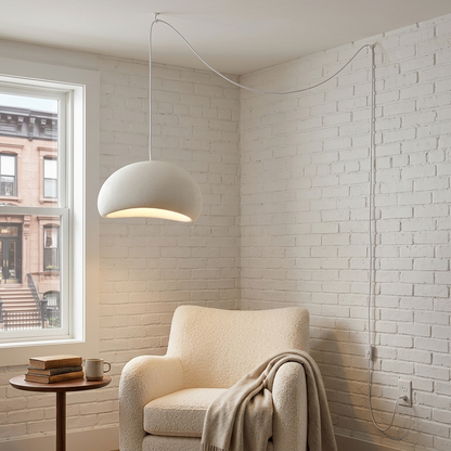 Thessaly cloud plug-in swag pendant light in White over a reading chair in an apartment living room